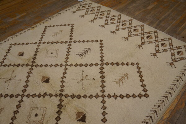 Shaggy ivory rug with a large brown geometric pattern covering a distressed wood plank floor.