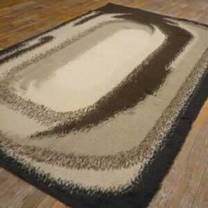 A high-pile rug with abstract brown and beige swirling bands lies on rustic wood flooring.