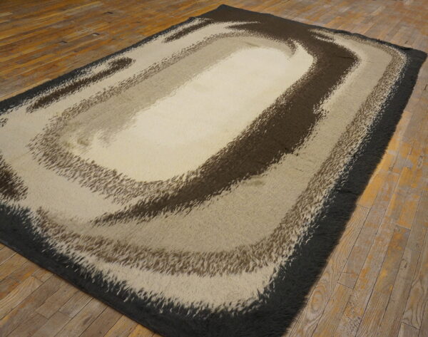 A high-pile rug with abstract brown and beige swirling bands lies on rustic wood flooring.