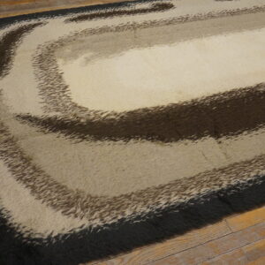 High pile rug featuring a swirling abstract design in black, brown, and cream on wooden floorboards.