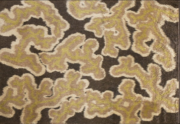 Textured rug displays abstract, feathered shapes in tan, olive green, and cream on dark brown.