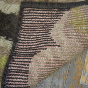 High-pile rug top in abstract brown and green folded over striped woven backing on distressed flooring.