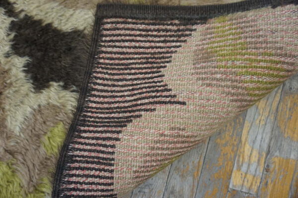 High-pile rug top in abstract brown and green folded over striped woven backing on distressed flooring.