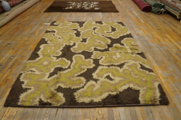 Shaggy brown, beige, and lime green abstract rug displayed on wide plank wood floors.
