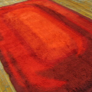 High pile shag rug in red, orange, and burgundy gradient colors on a plank wooden floor.