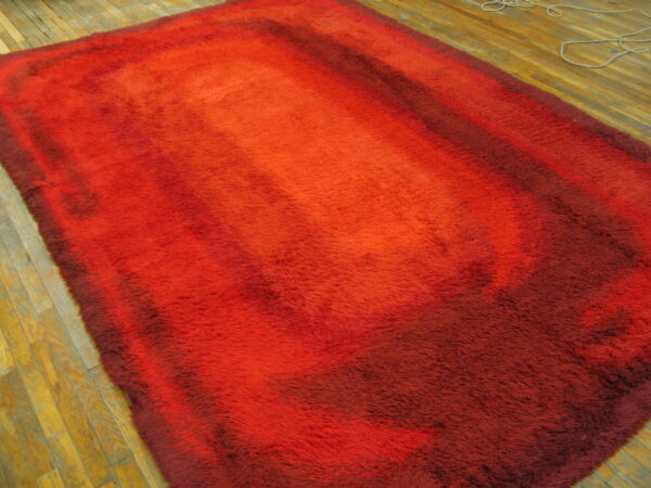 High pile shag rug in red, orange, and burgundy gradient colors on a plank wooden floor.