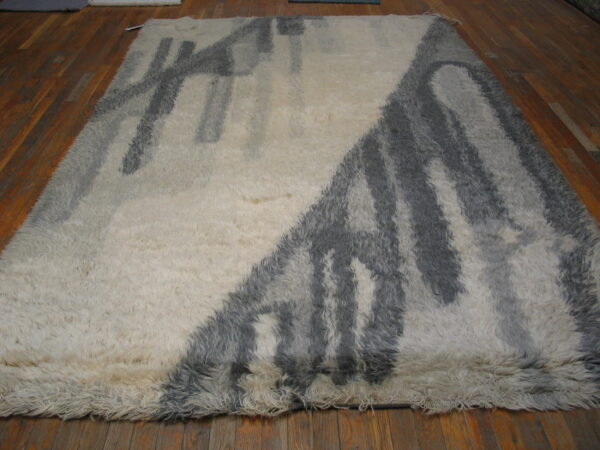 Shaggy, high-pile cream rug featuring a thick abstract grey pattern over reddish-brown wood planks.