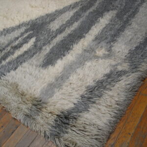 A thick, shaggy gray and cream rug featuring abstract stripes rests on wide plank wood flooring.