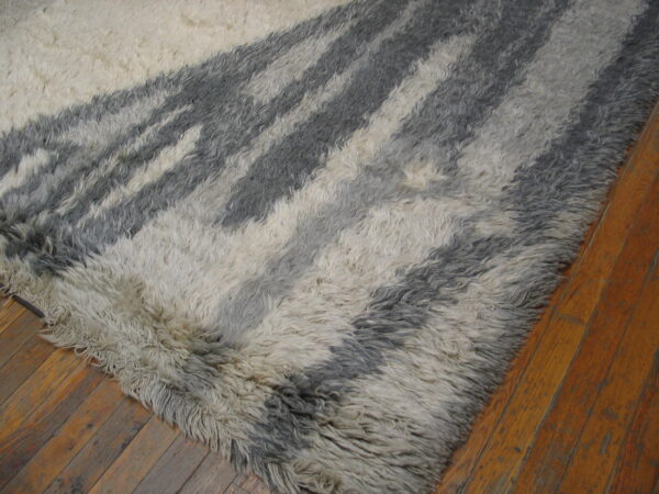 A thick, shaggy gray and cream rug featuring abstract stripes rests on wide plank wood flooring.