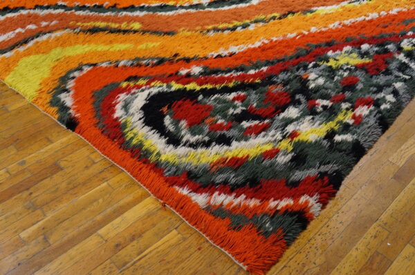 Multi-colored shag rug in red, orange, yellow, and dark green, resting on honey-toned wood floors.