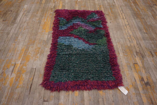 High-pile shaggy rug with magenta border and abstract green and blue pattern on distressed wood planks.