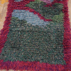 Mottled green, blue, and magenta shaggy rug with high pile sits on worn light wood flooring.