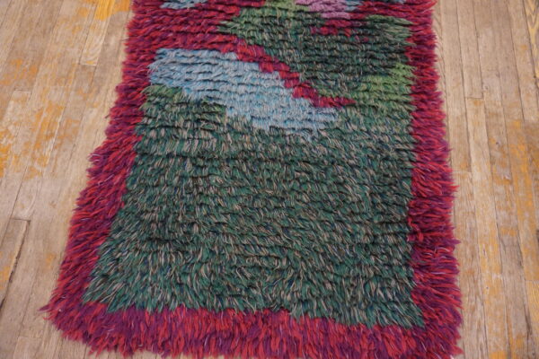 Mottled green, blue, and magenta shaggy rug with high pile sits on worn light wood flooring.