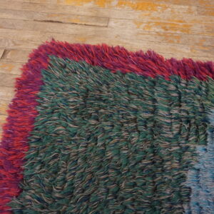A textured shaggy rug with color blocks in red, green, and light blue rests on peeling wood floor.