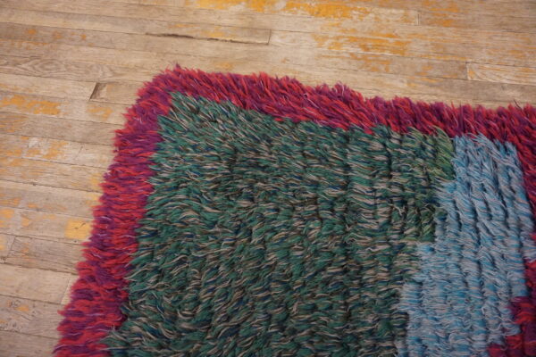 A textured shaggy rug with color blocks in red, green, and light blue rests on peeling wood floor.