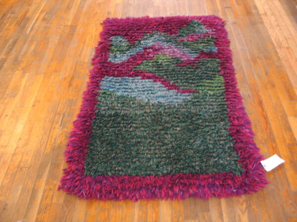 High-pile shag rug in abstract green, blue, and pink patterns framed by a magenta border on wood flooring.