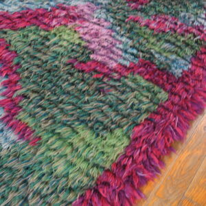 A vibrant, shaggy rug with pink, teal, and green diagonal color blocks lies on hardwood flooring.
