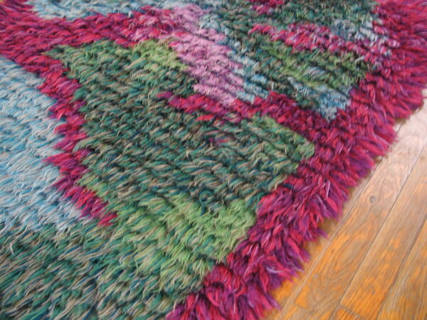 A vibrant, shaggy rug with pink, teal, and green diagonal color blocks lies on hardwood flooring.