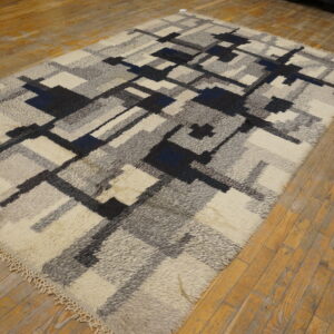 Shaggy rug with an abstract geometric pattern in off-white, gray, black, and blue on distressed wooden floors.