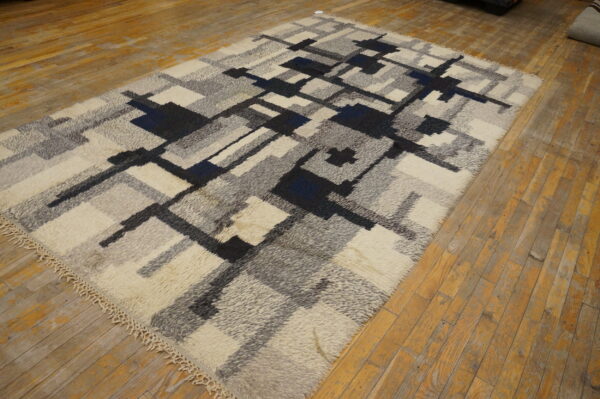 Shaggy rug with an abstract geometric pattern in off-white, gray, black, and blue on distressed wooden floors.