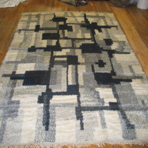High pile rug featuring abstract cream, gray, and black geometric designs rests on hardwood flooring.