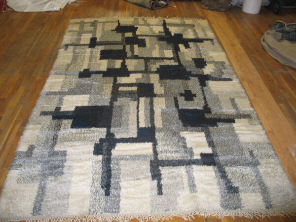 High pile rug featuring abstract cream, gray, and black geometric designs rests on hardwood flooring.