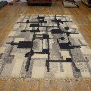 Textured high pile rug featuring gray, cream, and navy geometric blocks on a distressed wood floor.