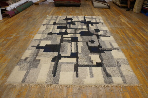 Textured high pile rug featuring gray, cream, and navy geometric blocks on a distressed wood floor.