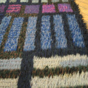 Shaggy blue, purple, pink, and white geometric rug detailing dark outlines, resting on hardwood flooring.