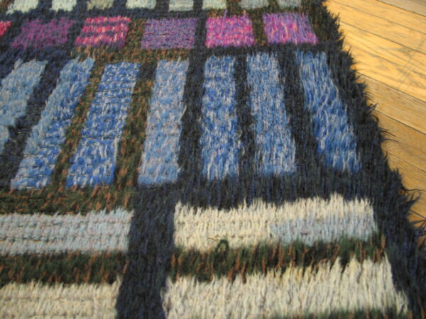 Shaggy blue, purple, pink, and white geometric rug detailing dark outlines, resting on hardwood flooring.
