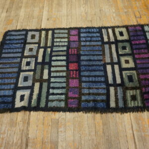 Dark blue, magenta, and teal geometric rug with a shaggy texture lies on rustic wood planks.