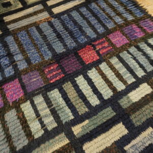 Chunky, high-pile rug with a multicolored geometric block pattern in blues, greens, purple, and red tones on wood floor.