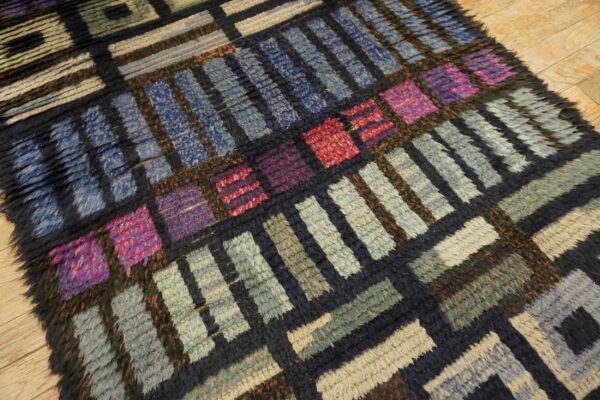Chunky, high-pile rug with a multicolored geometric block pattern in blues, greens, purple, and red tones on wood floor.