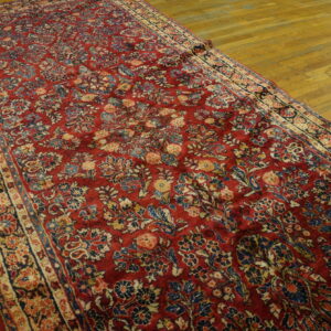 Long, red, low-pile rug with a detailed multicolored floral pattern displayed on a wooden floor.