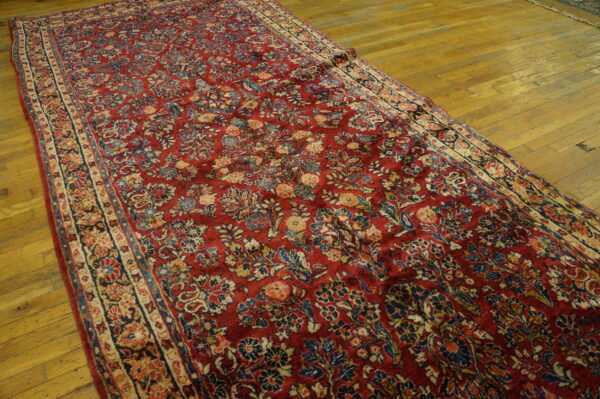 Long, red, low-pile rug with a detailed multicolored floral pattern displayed on a wooden floor.