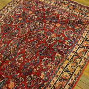 Ornate red rug with faded blue and beige floral designs rests on distressed wooden flooring.