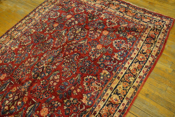Ornate red rug with faded blue and beige floral designs rests on distressed wooden flooring.