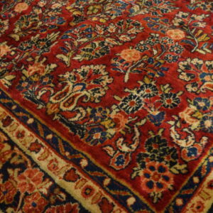Detailed view of a classic red rug with intricate blue, cream, and peach floral patterns and borders.