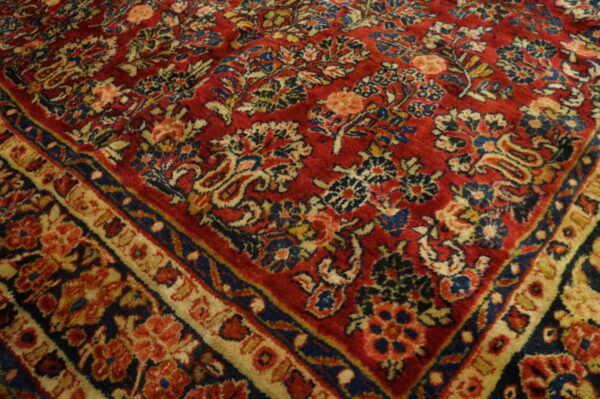 Detailed view of a classic red rug with intricate blue, cream, and peach floral patterns and borders.