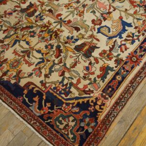 Cream rug with an intricate vine pattern and a bold navy border rests on worn wood plank flooring.