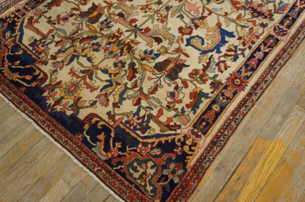 Cream rug with an intricate vine pattern and a bold navy border rests on worn wood plank flooring.