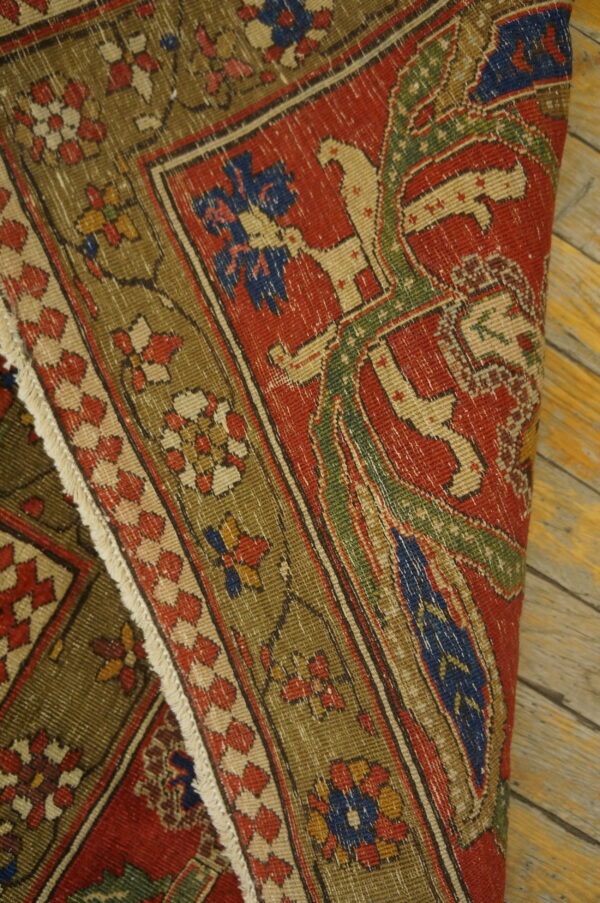 A low-pile red, olive, and blue patterned rug with fringes is rolled on rustic wood planks.