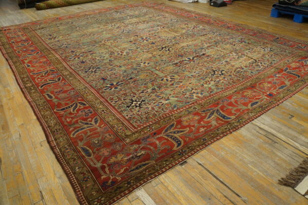 A large, faded floral rug featuring a pale green field and rich red borders rests on wood floors.