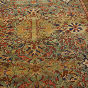 A densely patterned rug with a variegated sage field and ornate floral motifs in red, navy, and gold.