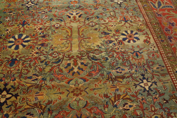 A densely patterned rug with a variegated sage field and ornate floral motifs in red, navy, and gold.