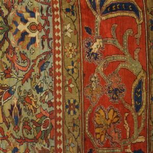 Intricate floral rug pattern in deep red, olive green, and blue sits on light wooden flooring.