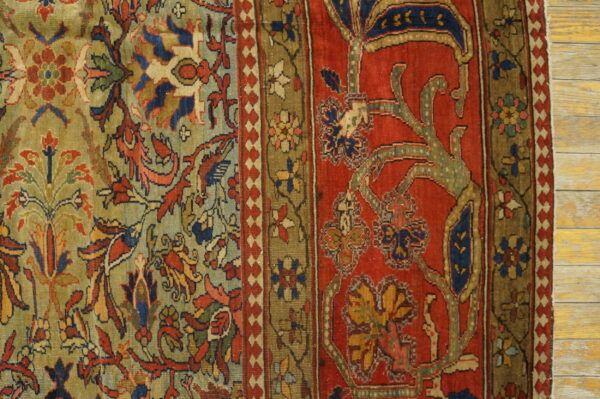 Intricate floral rug pattern in deep red, olive green, and blue sits on light wooden flooring.