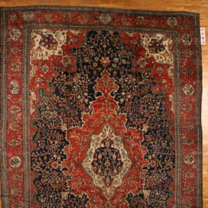 Detailed navy blue and red traditional rug with an intricate central motif, displayed on wood plank flooring.