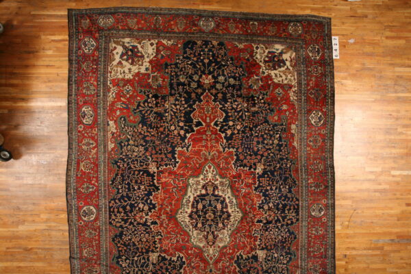 Detailed navy blue and red traditional rug with an intricate central motif, displayed on wood plank flooring.