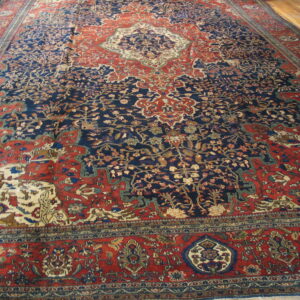 Ornate navy blue and rust red traditional rug with an intricate floral pattern on wood flooring.
